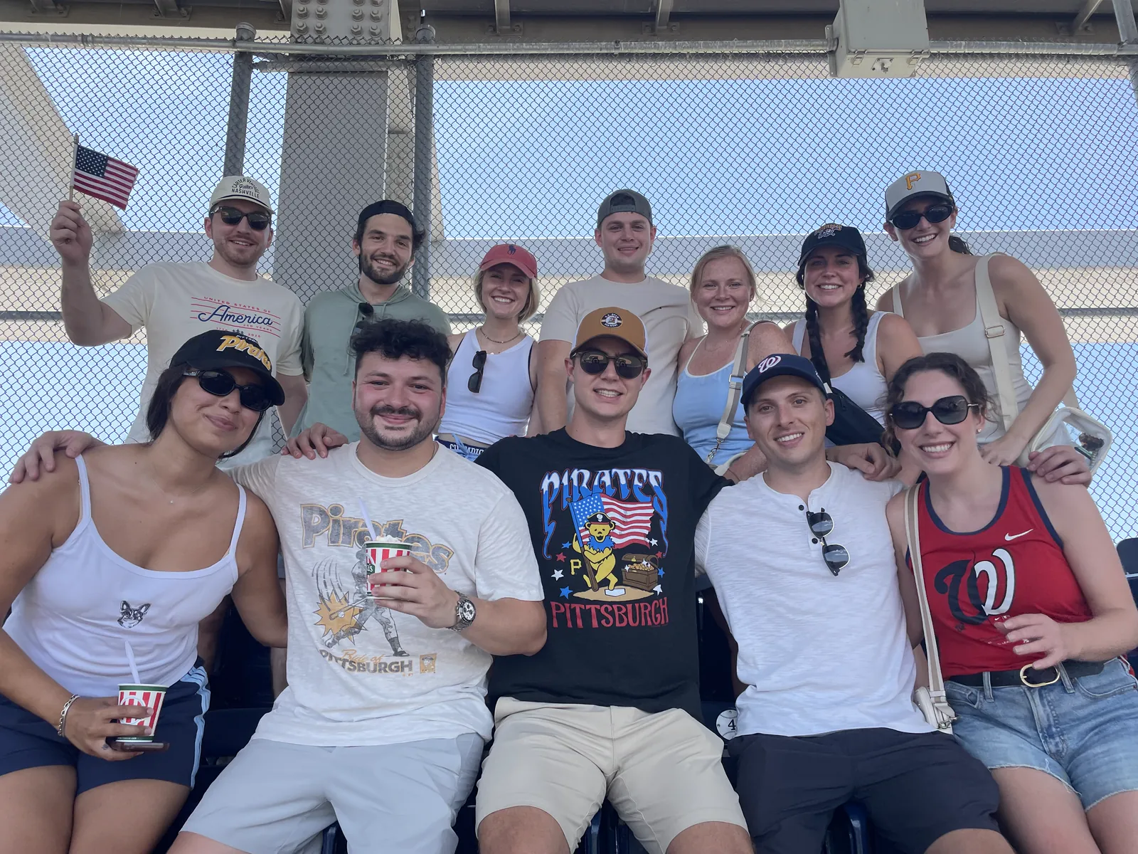 A big group of friends in red, white, and blue at a ballgame, one waving a small American flag