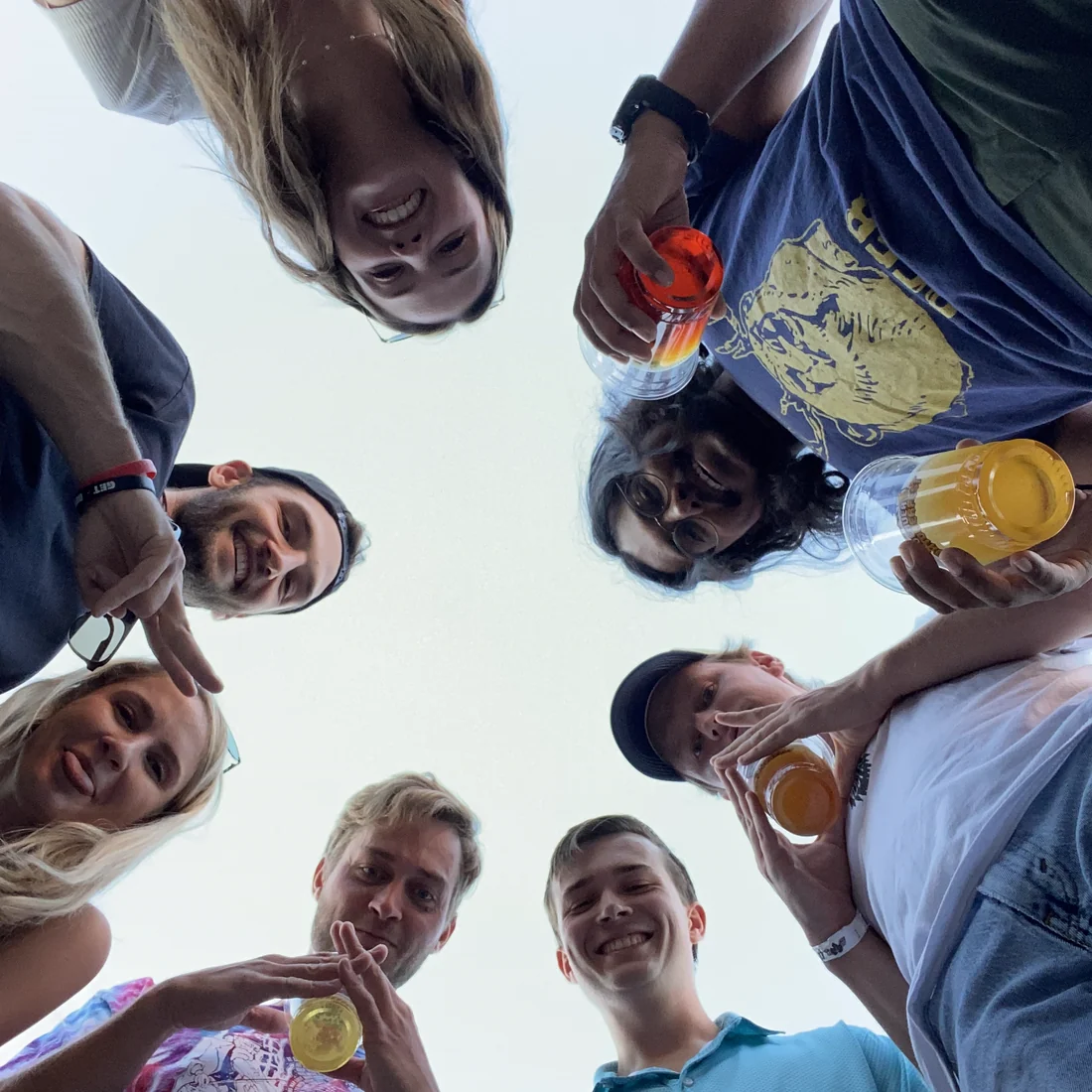 Kaitlyn, Jack, and friends in a circle, grinning down at the camera with drinks in hand