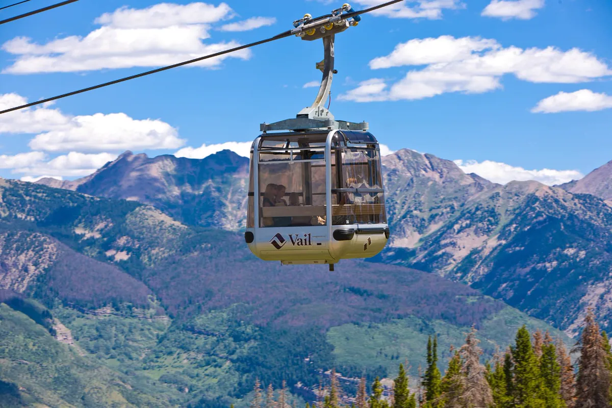 A Vail gondola cabin gliding above green summer mountains